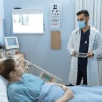 Doctor wearing face mask consulting with a patient in a hospital room, highlighting healthcare safety