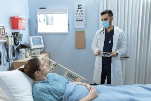 Doctor wearing face mask consulting with a patient in a hospital room, highlighting healthcare safety