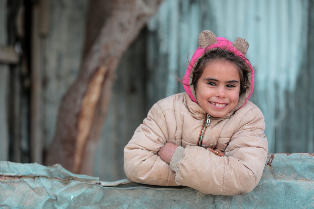 Charming portrait of a young girl smiling warmly in Gaza, dressed in a pink hooded jacket