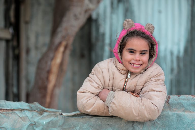 Home 36 Charming portrait of a young girl smiling warmly in Gaza, dressed in a pink hooded jacket