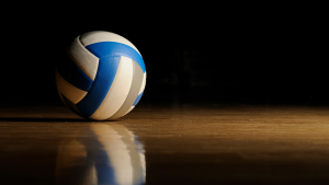 A blue and white volleyball rests on a wooden floor against a dark background