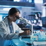 A laboratory researcher examines a sample through a microscope