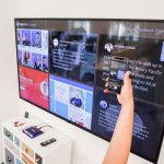 A woman uses a smartphone to scan a QR code on a digital wall display indoors
