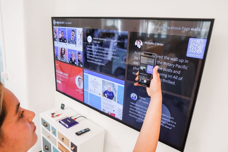 A woman uses a smartphone to scan a QR code on a digital wall display indoors