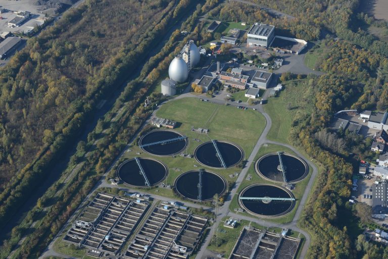 Aerial photograph of a wastewater treatment plant surrounded by autumn trees, showcasing ecological and industrial elements