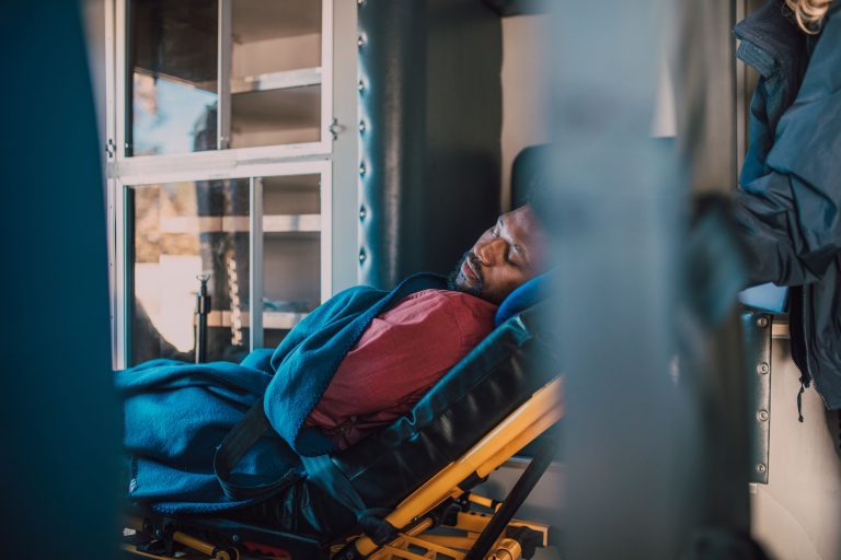 An adult man rests on a stretcher under a blue blanket
