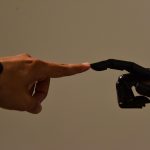 A human finger touches a black robotic finger, an illustrative robot interaction