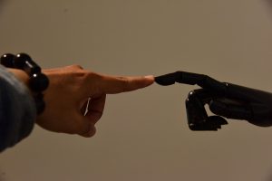A human finger touches a black robotic finger, an illustrative robot interaction
