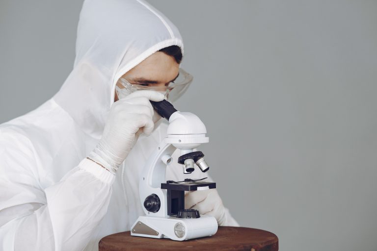 Home 18 Scientist in protective gear using a microscope, focused on research and analysis